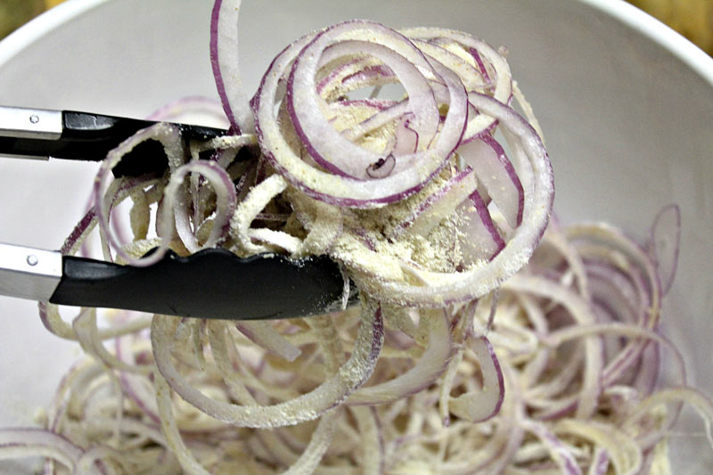 Sliced red onion in bowl mixing with seasoning for bbq chicken bites