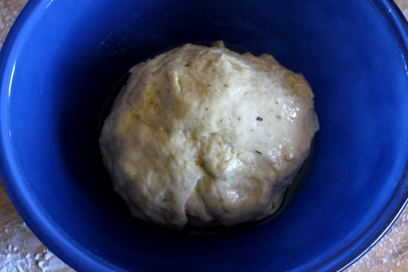 Dough rising in blue bowl with olive oil