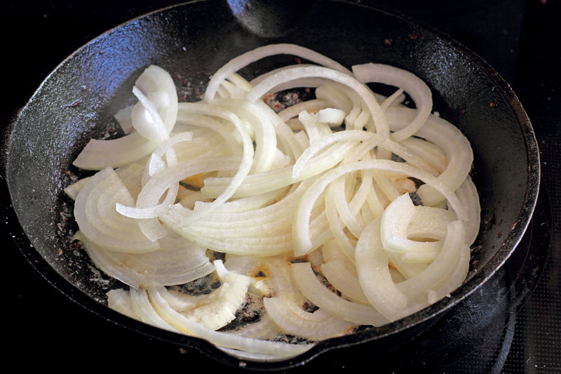 caramelizing onions in cast iron skillet with butter sausage and artichoke